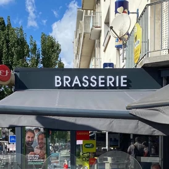 Auvent gris déployé au-dessus de la terrasse, surmonté du bandeau « Brasserie ».