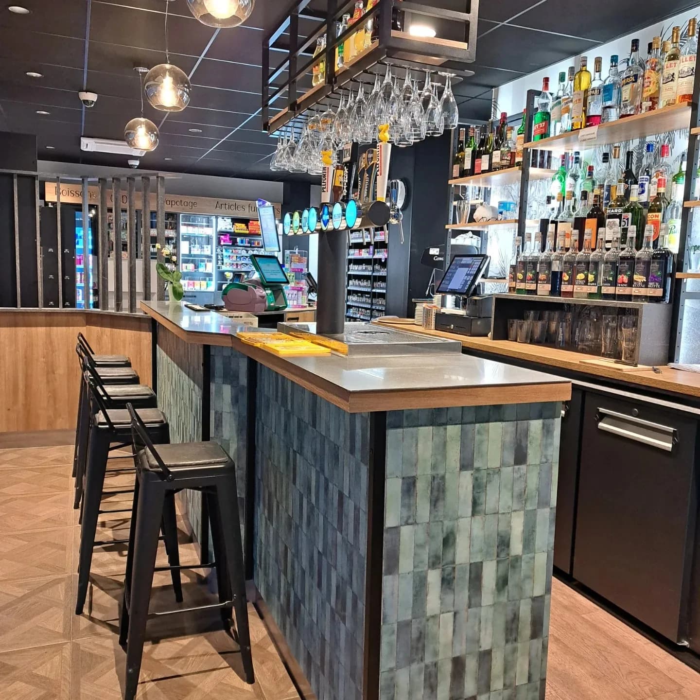 Le comptoir habillé de zellige vert, la colonne de becs à bière, les tabourets et, au fond, le rayon tabac.