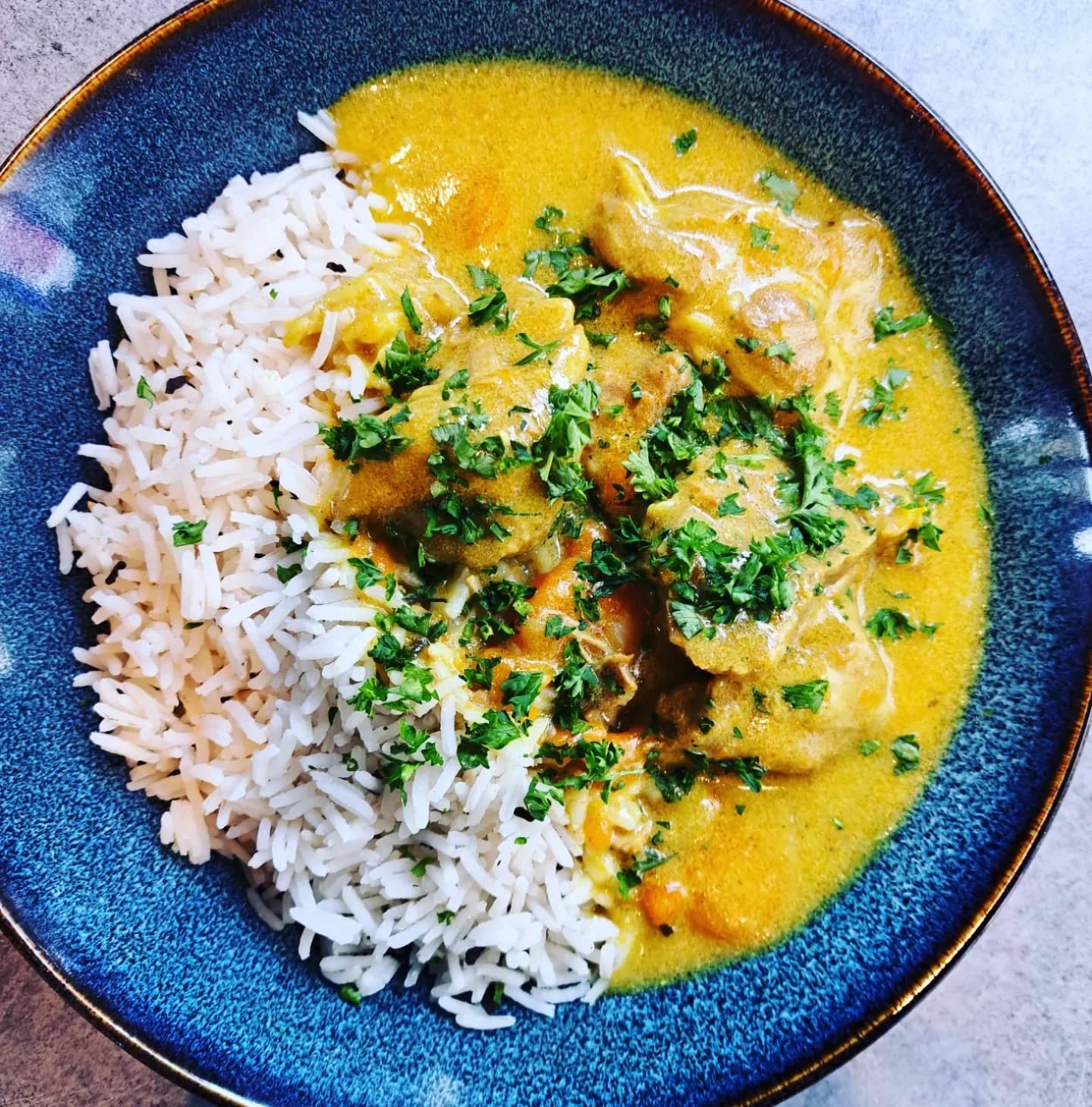 Curry de porc au lait de coco et riz parfumé, servi dans une assiette bleue.
