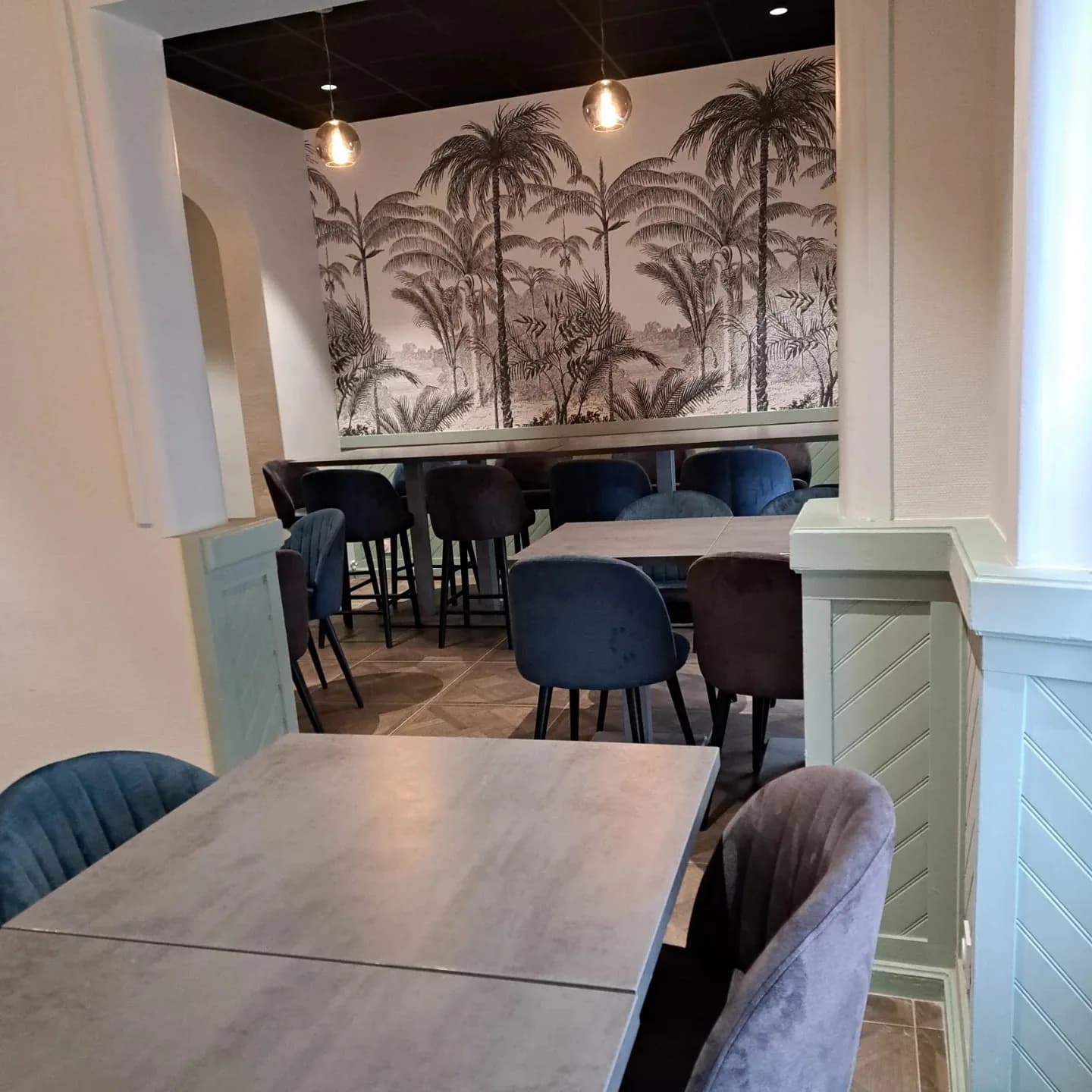 L'alcôve de la salle, boiseries vert d'eau et tables carrées face à la fresque de palmiers.